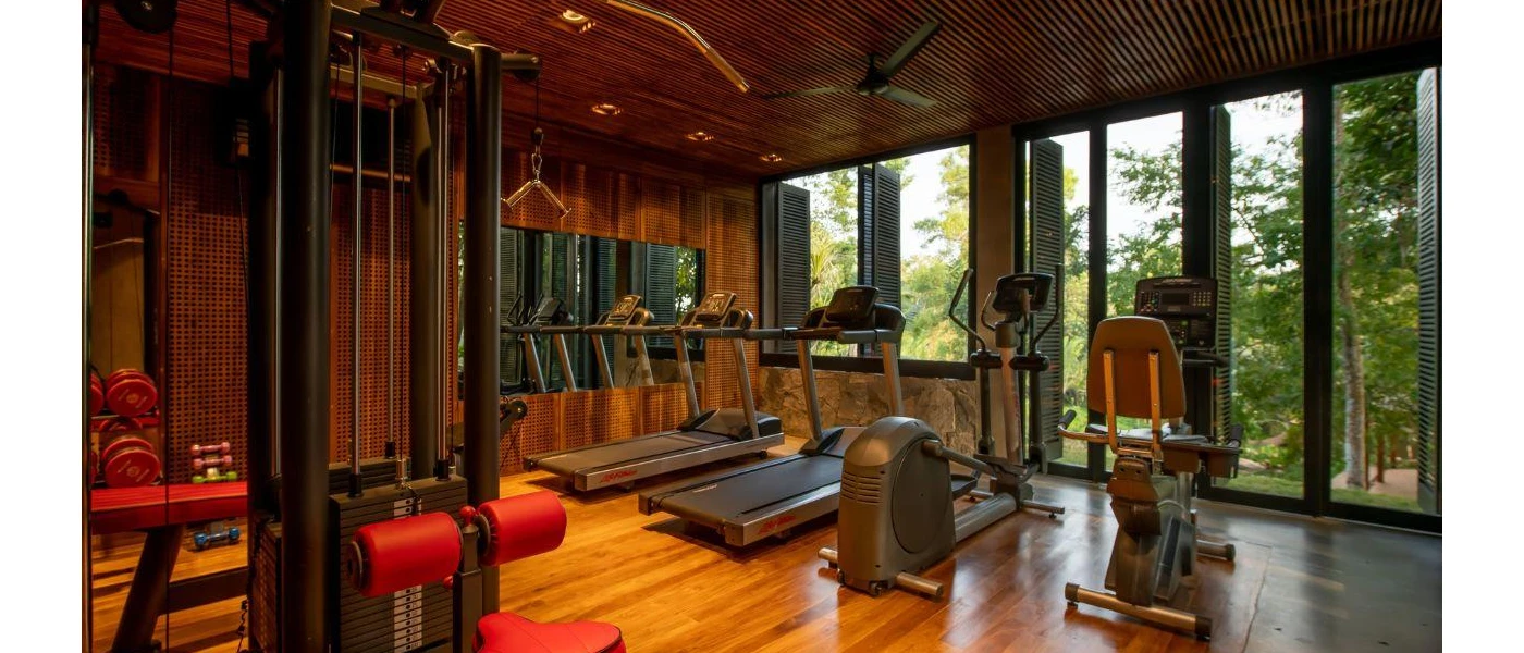 Gym with treadmills, exercise bike and weight machines with full-length windows with a jungle view