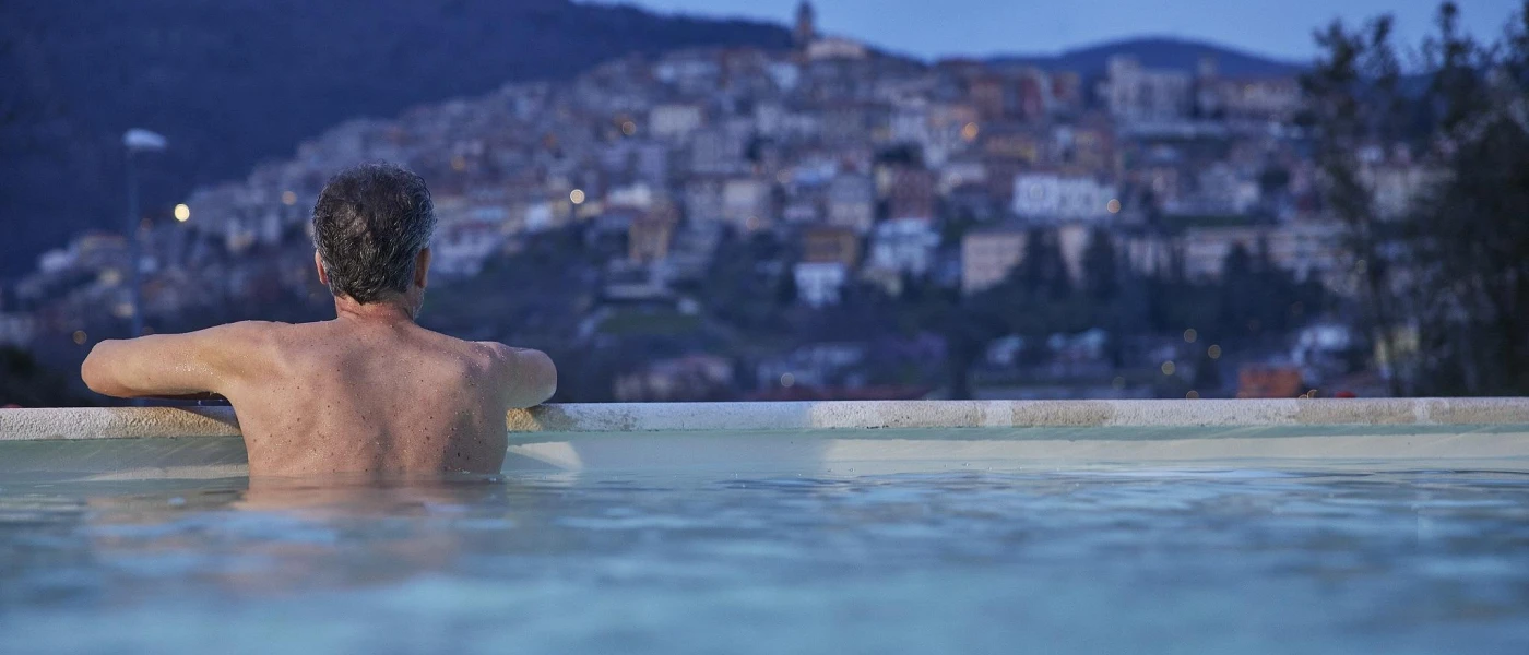 Man in a swimming pool looks out towards the hillside town of Fiuggi as the sky darkens