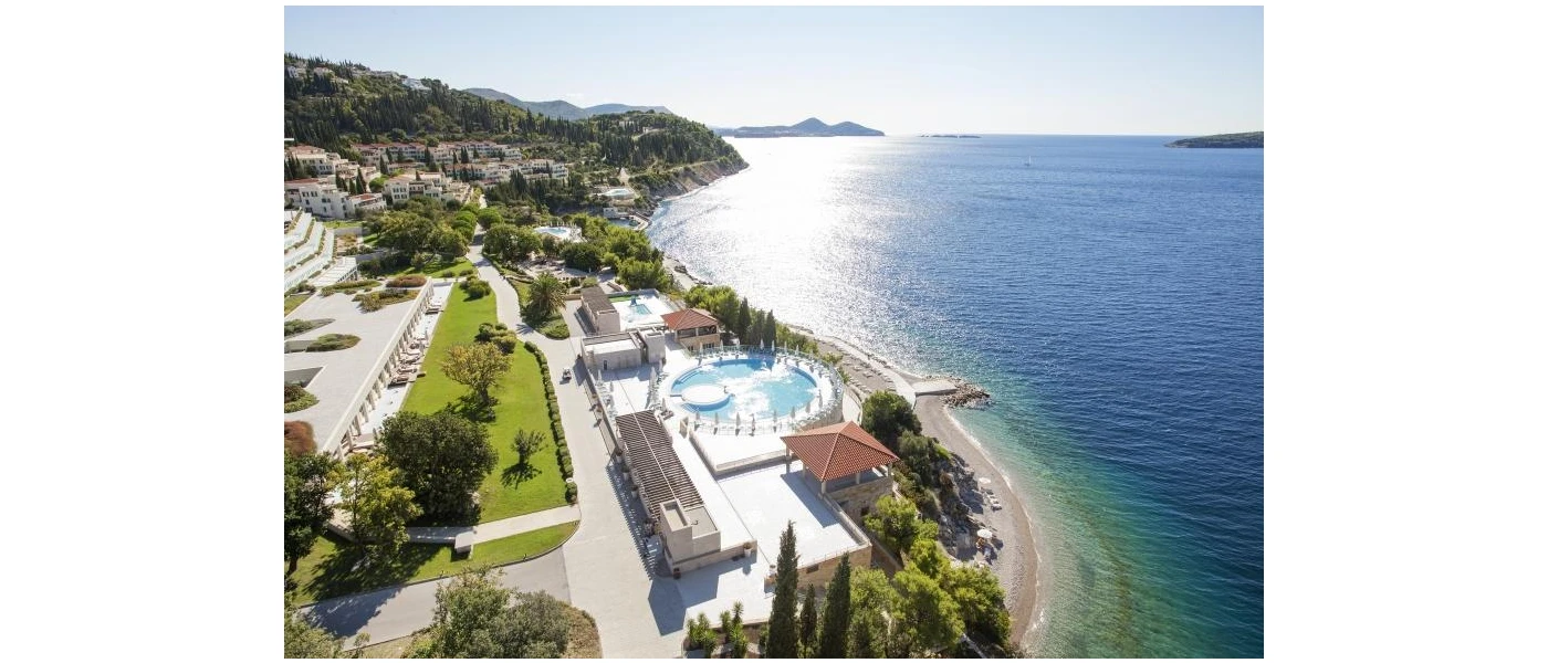 Green landscaped grounds and a circular pool overlooking the sea, as seen from above