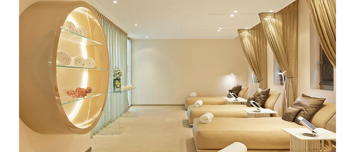 Chic relaxation room with gold daybed, cushions and curtains, a glass table with candles and a tablet on each bed