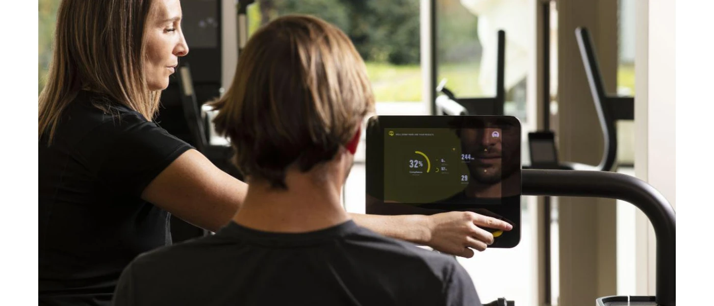 Man sits in front of gym equipment as a professional adjusts the settings in front of him