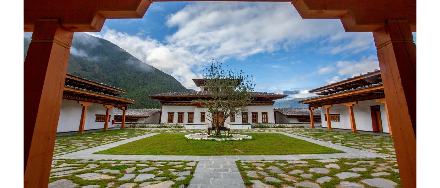Monastery courtyard with a tree at the centre and green hills in the background under a cloudy blue sky