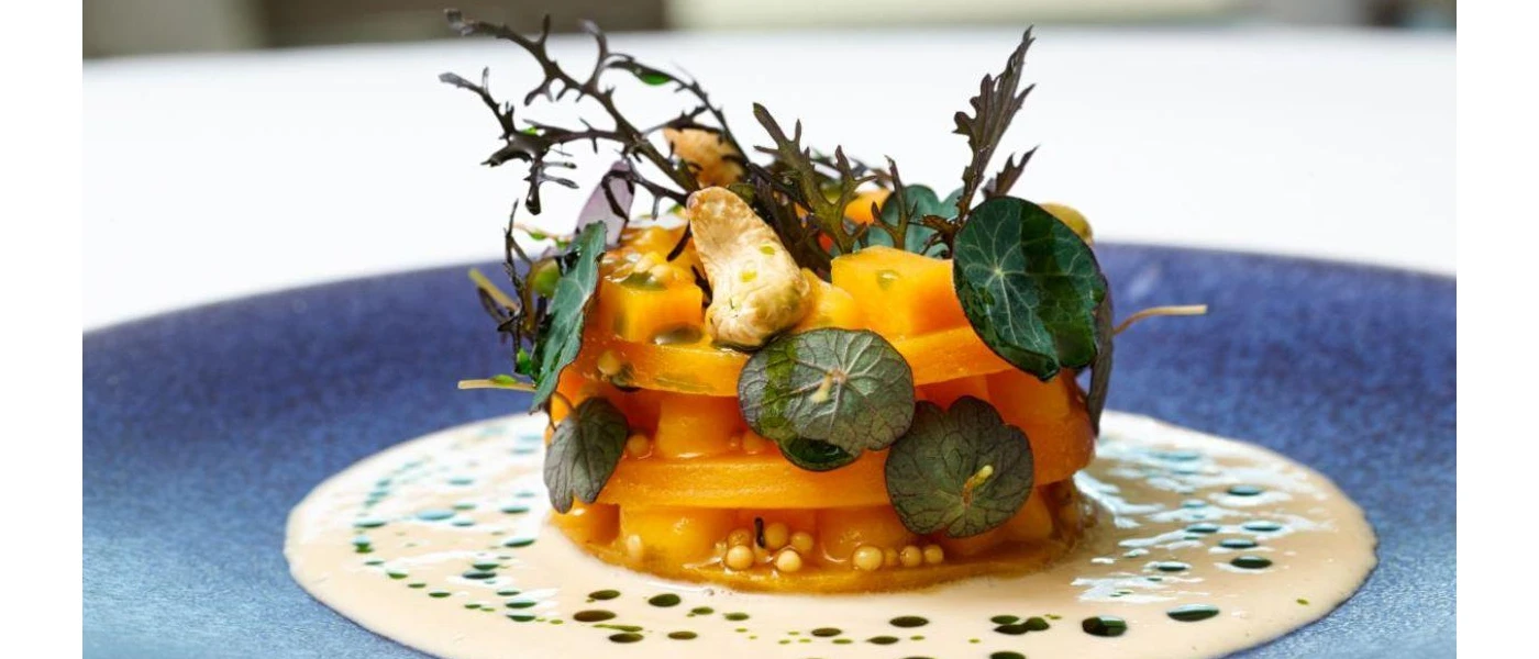 Intricately presented orange pile of food on top of a white sauce, with herbs as a garnish