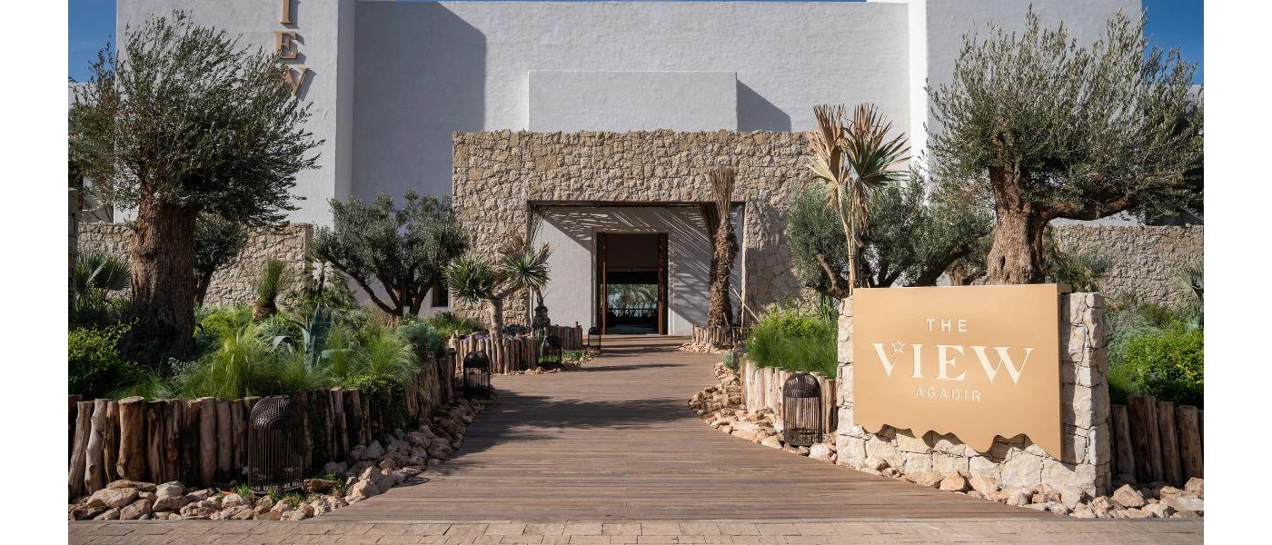 White building surrounded by trees and shrubs with a sign reading The View Agadir at the entrance