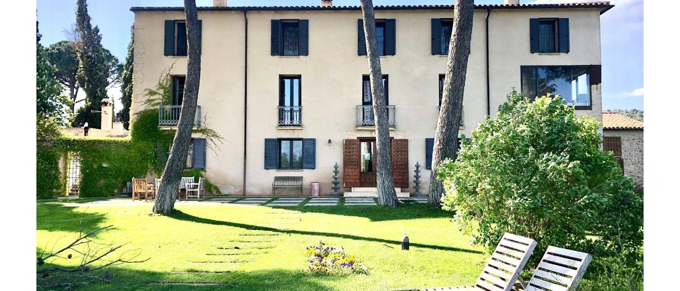 Rustic cream farmhouse with black window shutters in a lush green garden