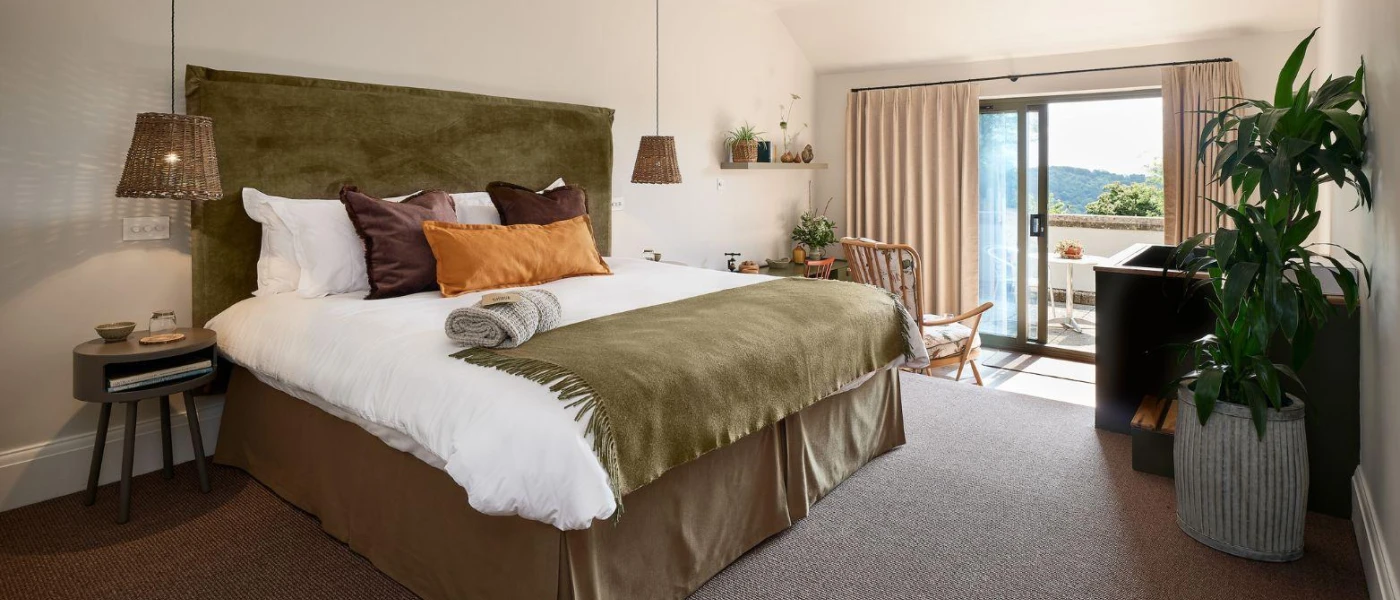 Modern hotel room with orange, grey and taupe soft furnishings, a large plant and double doors leading outside