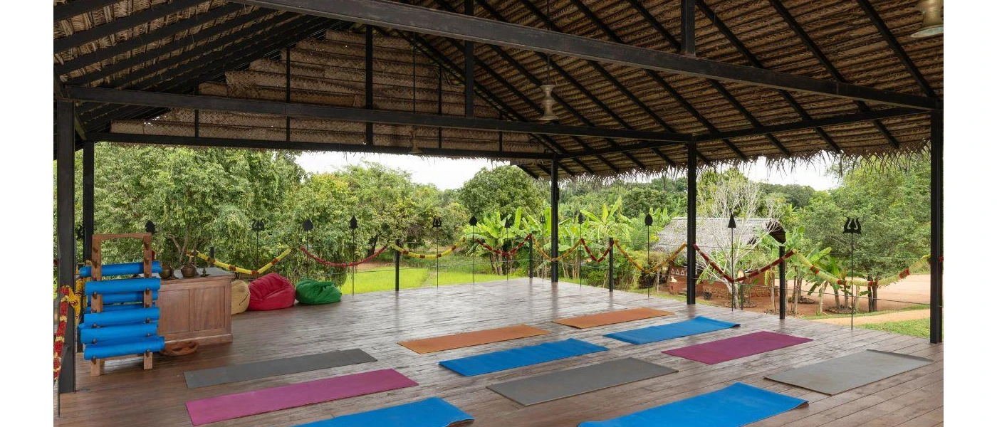 An open-sided yoga pavilion set up for a class with blue and pink mats laid out on a wooden decked floor