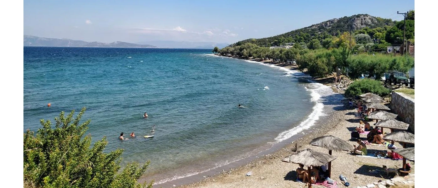 Small bay with thatched umbrellas and a rocky shoreline, surrounded by green hills