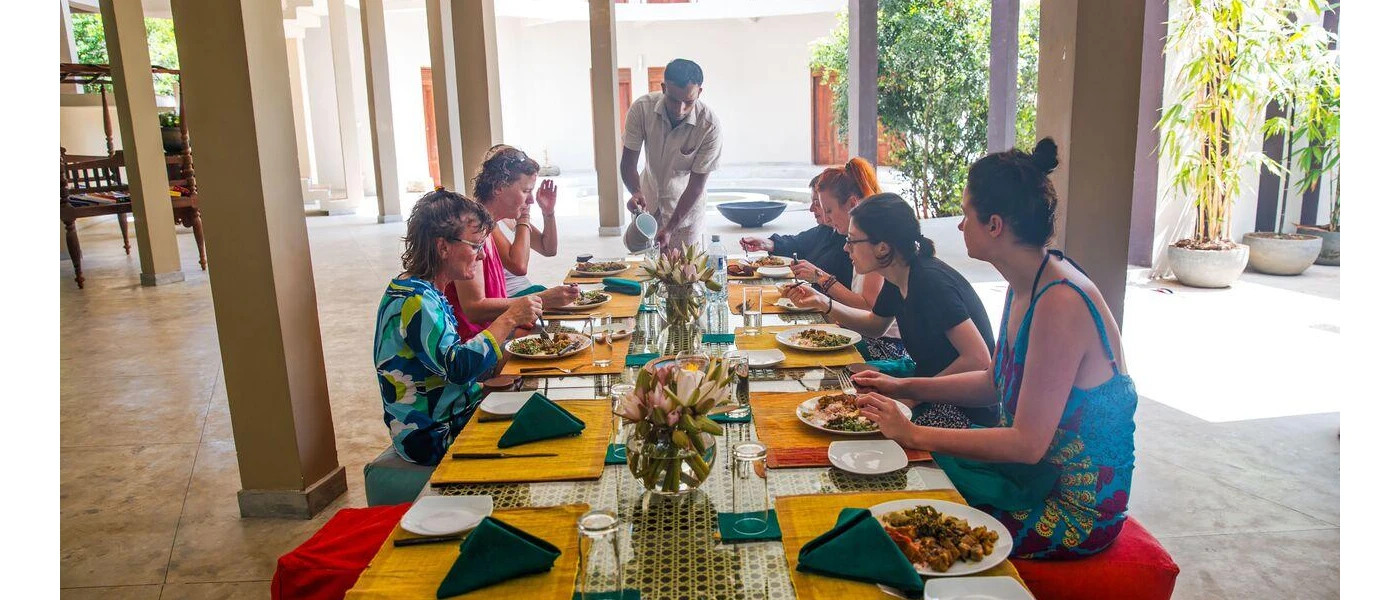 Group of women sitting around a colourful table eating as a staff member pours a drink at the end