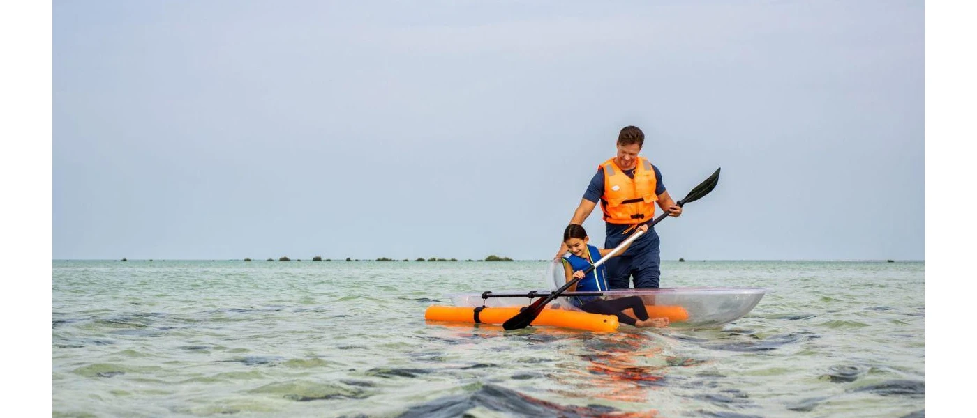 Father and daughter paddle in a glass-bottom rounded boat in the ocean