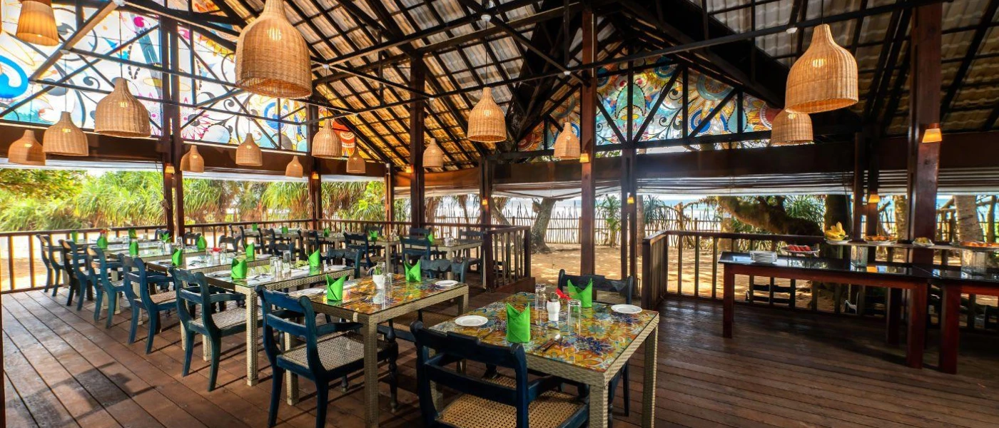 Airy dark-wood restaurant with open sides, rattan lantern-style pendant lights and tables with floral tiled tops