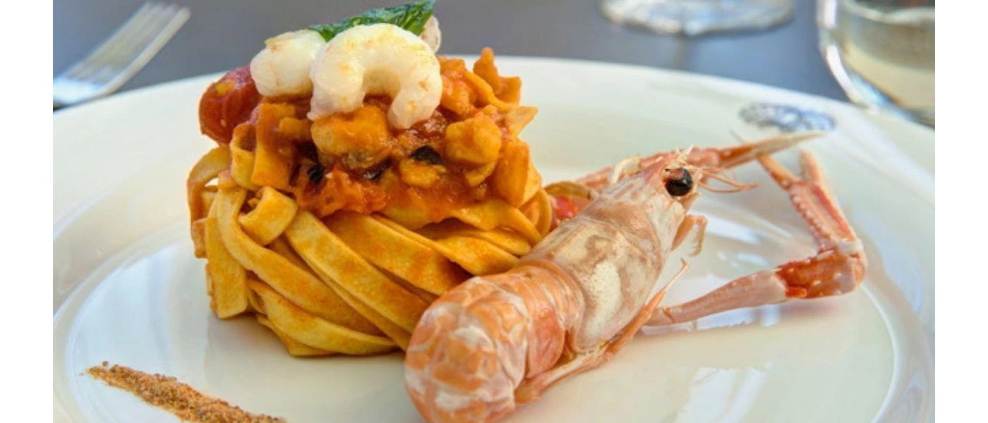 A mound of pasta on a white plate topped with prawns with a prawn that hasn't been shelled to one side