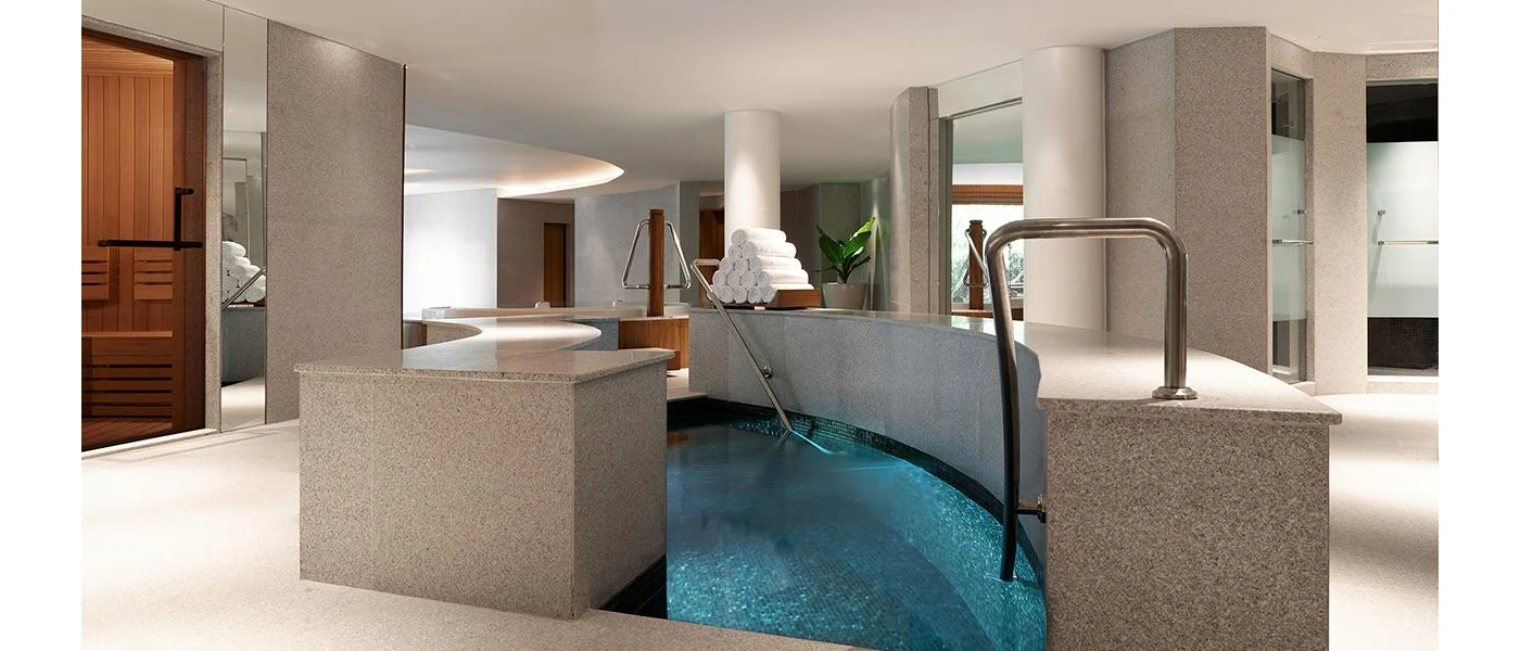 Steps into an indoor pool in a softly lit room, with a pyramid of white towels on a surface and a tropical plant in the background