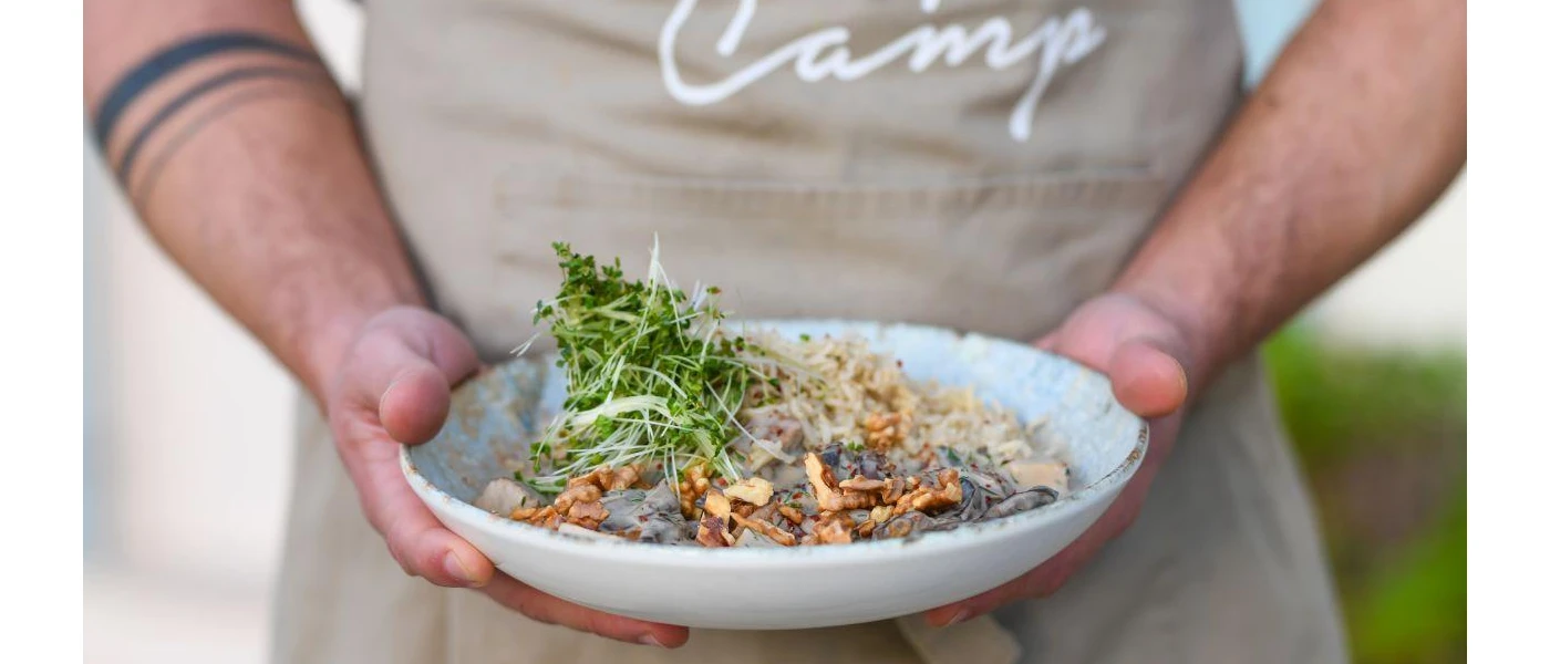 Man in a cream apron holds a white bowl with nutritious looking food topped with salad