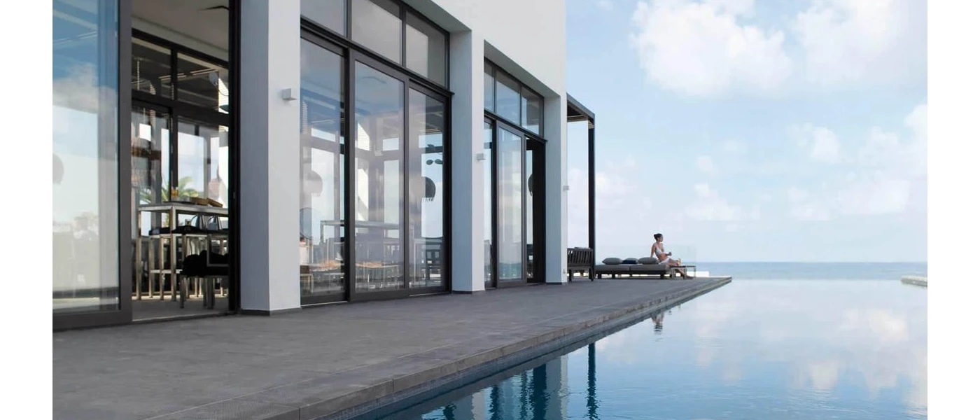 Infinity pool looking over the ocean next to a contemporary glass-windowed white building