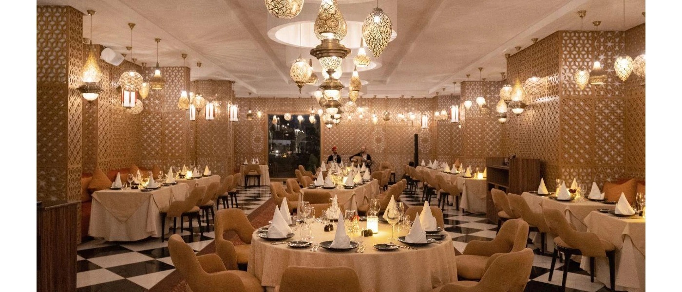 Lantern-lit restaurant with intricately patterned pillars, a black and white chequered floor and tables with gold chairs and beige tablecloths