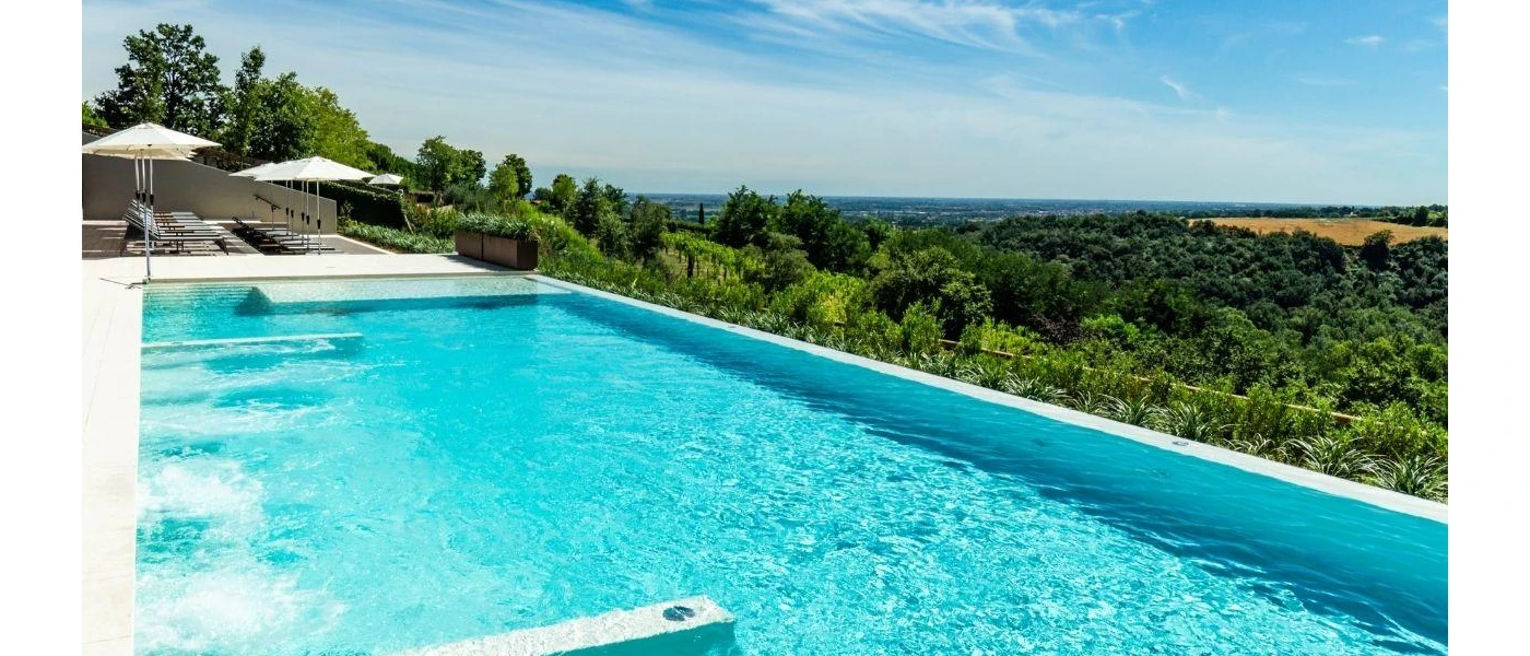 Swimming pool overlooking the green Italian countryside, next to white umbrellas and loungers