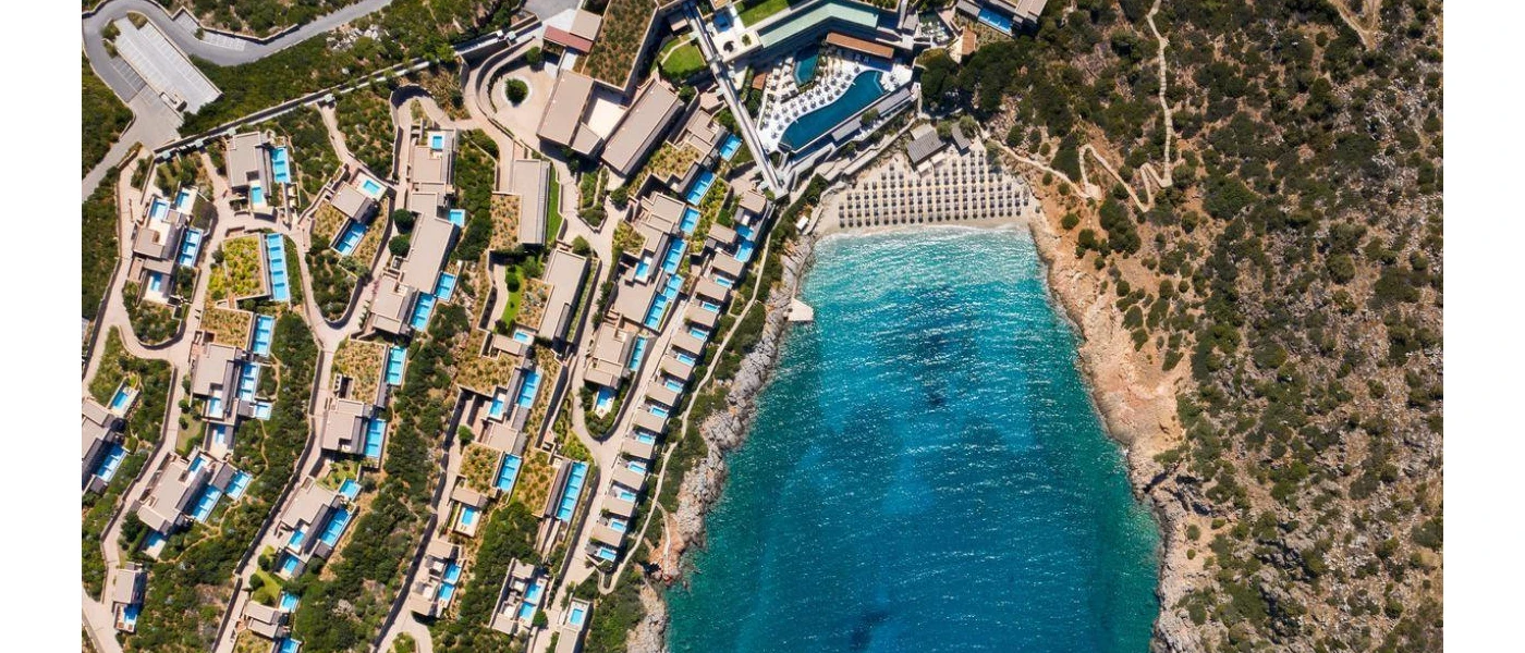 Aerial view of a turquoise cove surrounded by hills and low-rise whitewashed buildings 