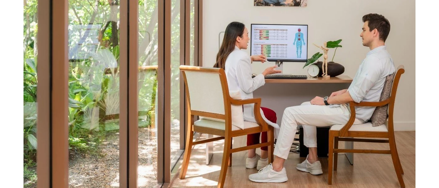 Woman in a white lab coat explains findings on a computer screen as a guest looks on next to her