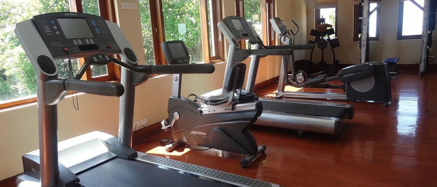 Treadmills in a gym with a shiny floor and windows overlooking tropical greenery
