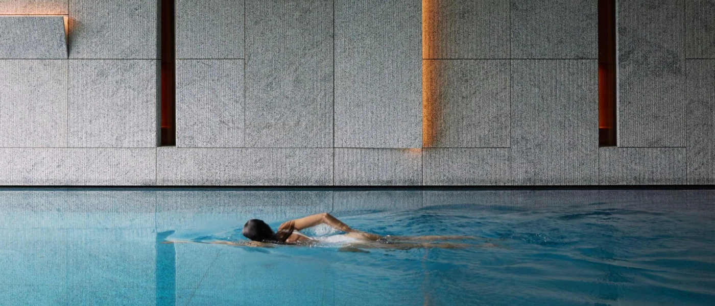 Woman doing front crawl in an indoor swimming pool in a room with tiled walls