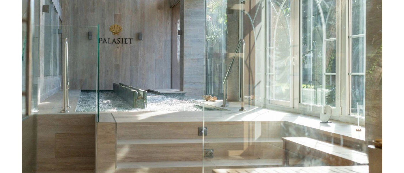 Room with sunlight beaming through the windows, and steps into a whirlpool bath surrounded by wood-panelled walls