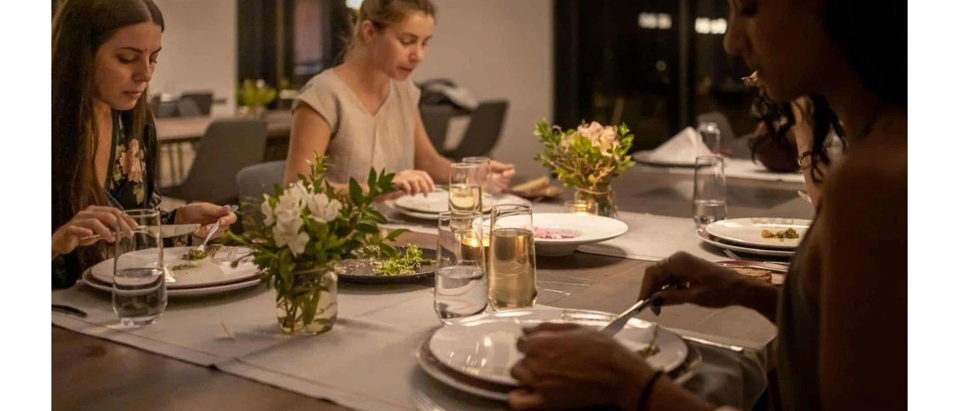 Group enjoy a meal in a softly lit restaurant with vases of white flowers on the table