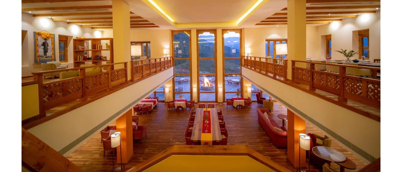 Red cushioned chairs in a restaurant setting, overlooking a fire pit and green hills 