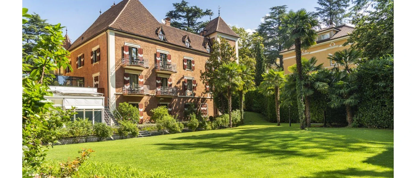 Landscaped grounds in front of a red-brick building with a tiled roof under a blue sky
