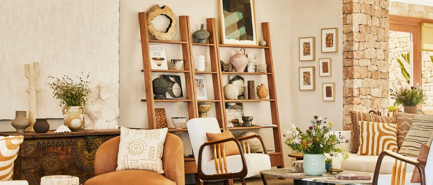 White-walled room with stone finishes, wooden shelving with ornaments, terracotta seating and potted plants