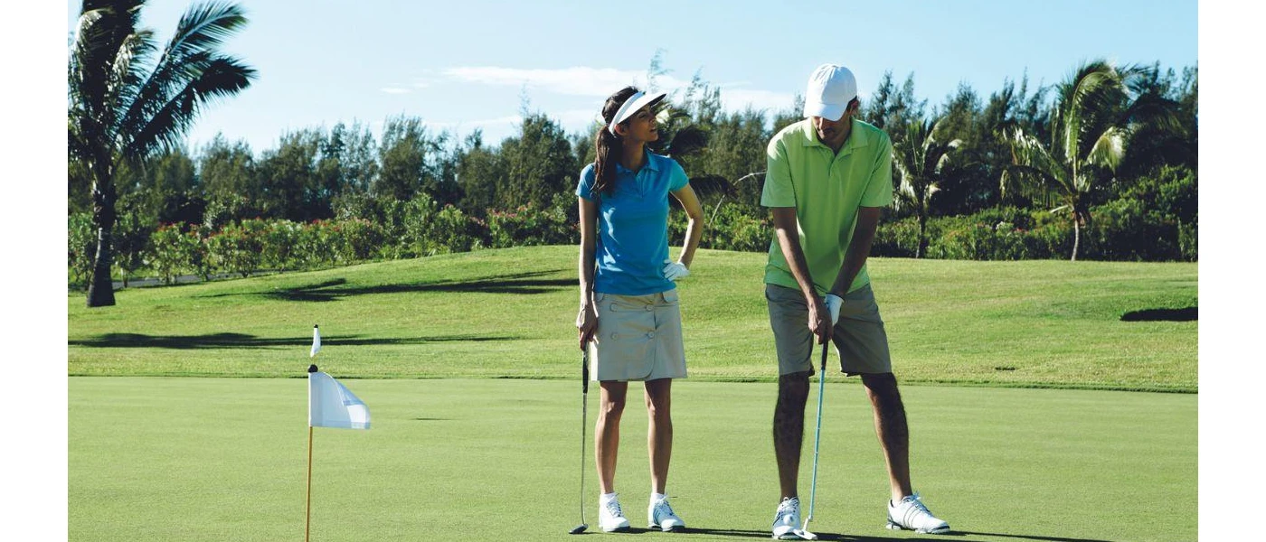 Man and woman in golf attire on a course backed by greenery