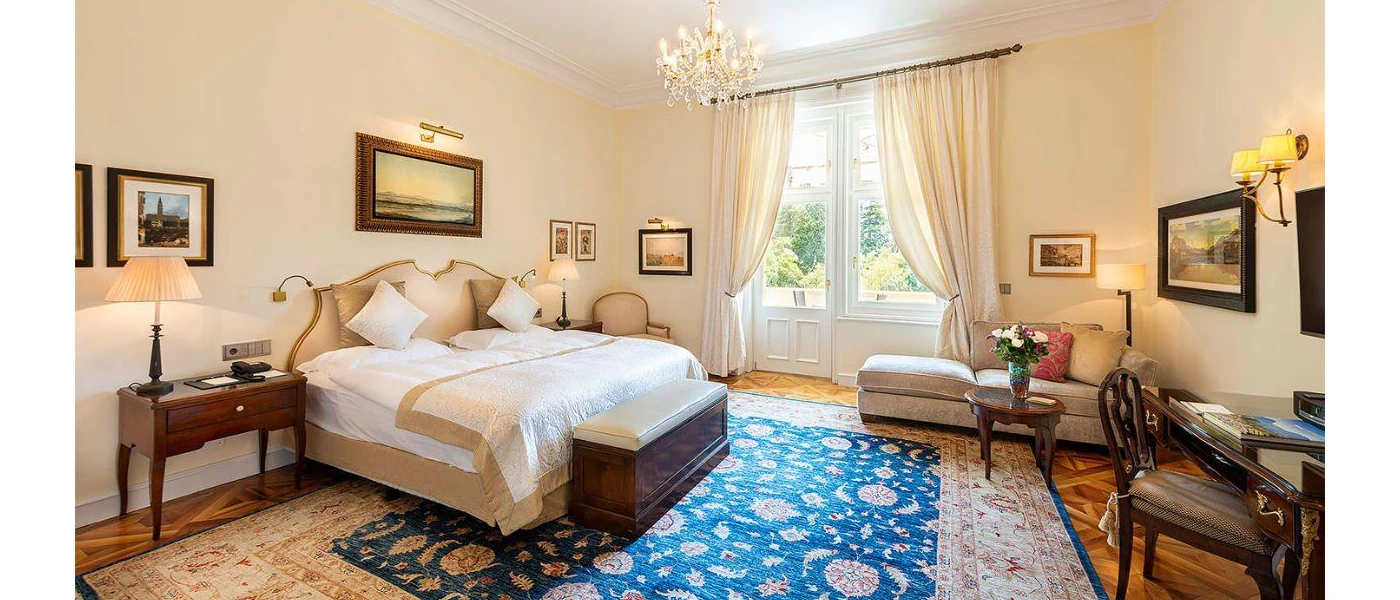Grand hotel room with neutral walls, dark-wood furniture, a glittering chandelier and patterned rug
