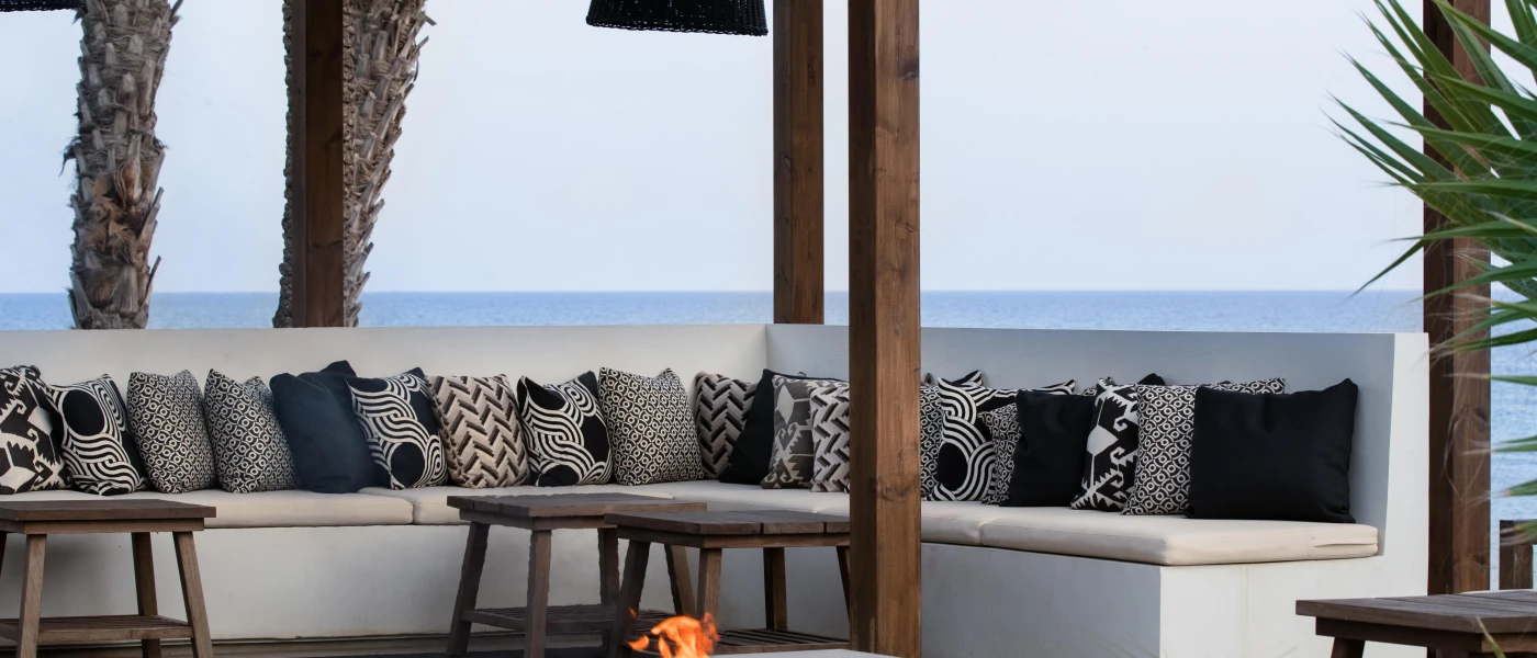 Stylish monochrome cushions on a white sofa next to a fire pit and covered by a dark-wood pergoda