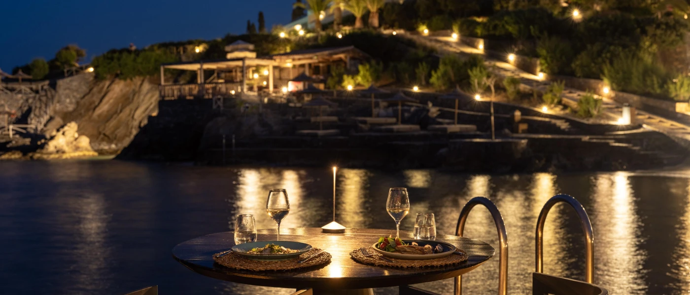 Oceanfront table for two looking over to a twinkling green hillside under a night sky