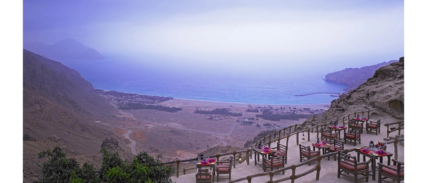 Mountaintop restaurant terrace with wooden furniture and red cushions, overlooking the ocean and resort below