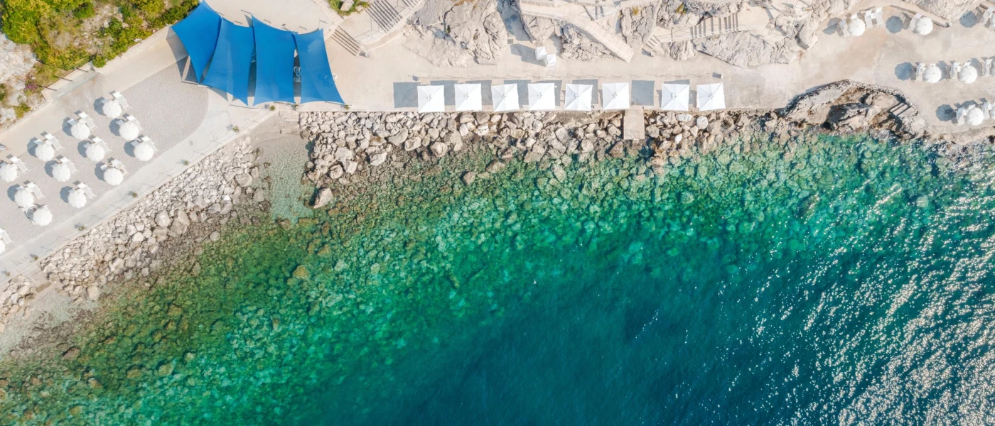 Paved terrace with loungers and umbrellas overlooking a rocky shore and clear blue sea