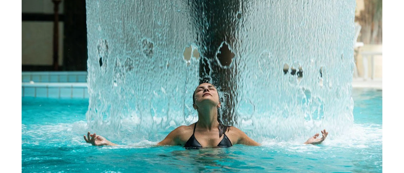 Woman in the thermal pool standing under a fountain of water