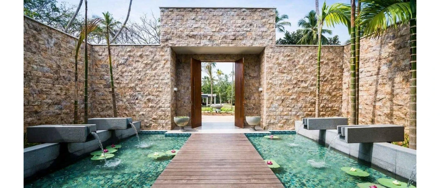 Courtyard with stone walls and a wooden jetty suspended over a pool, with lily pads floating in it