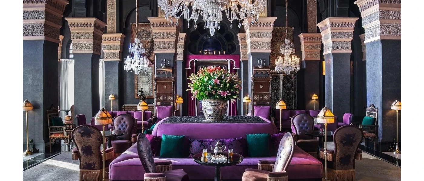 Purple cushioned seating area with other surrounding chairs in a room with a grand chandelier and patterned pillars