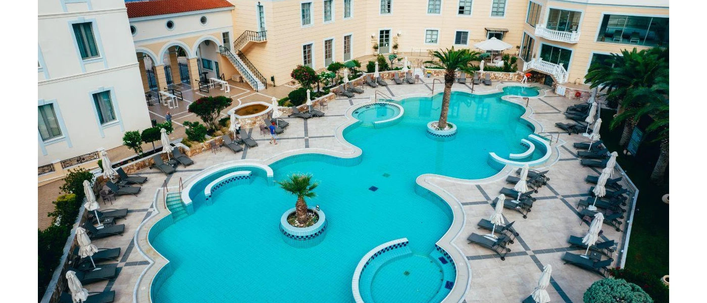 Swimming pool with rounded edges surrounded by palms, black loungers and 