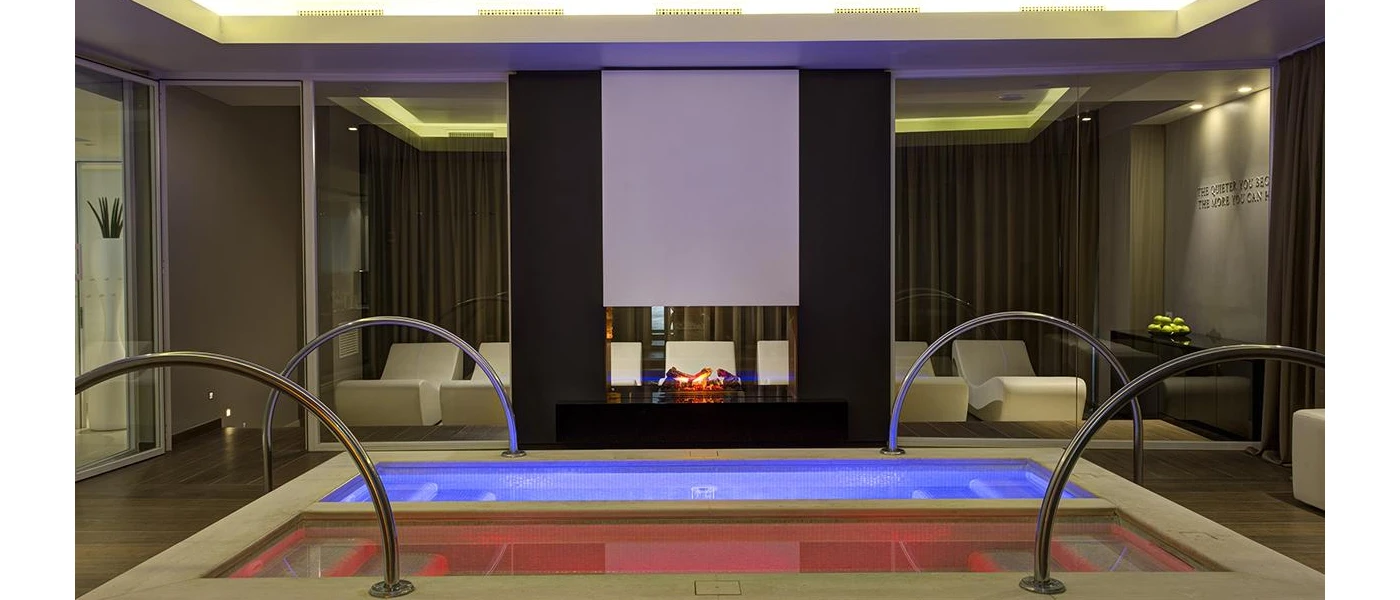 Indoor twin pools with stepped access lined with cream cube-like loungers and dark-wood walls