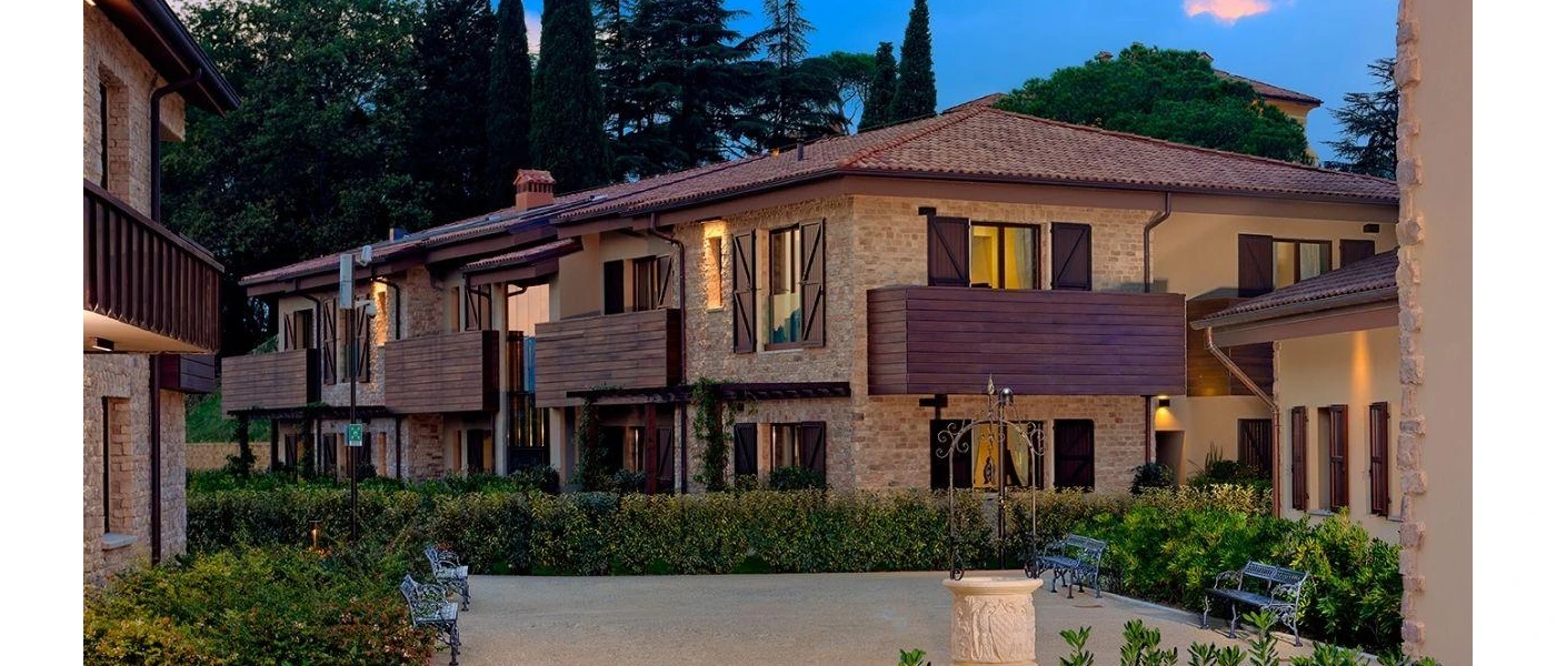 Buildings with terracotta roof tiles and stone walls, overlooking a courtyard framed by bushes