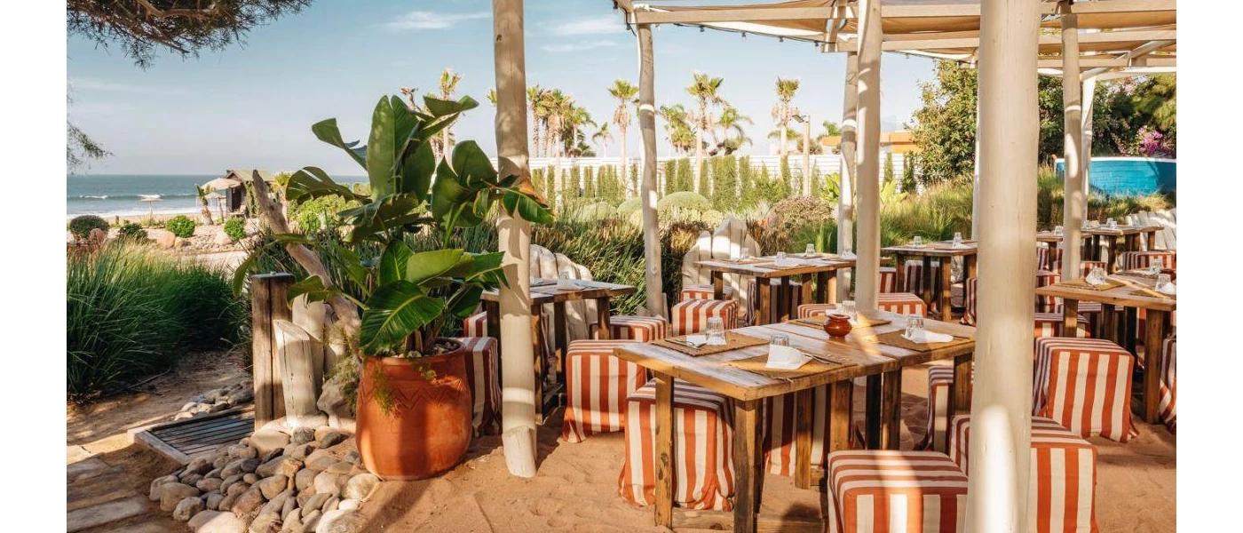 Outdoor covered seating area with orange and white striped cushions and a sea view