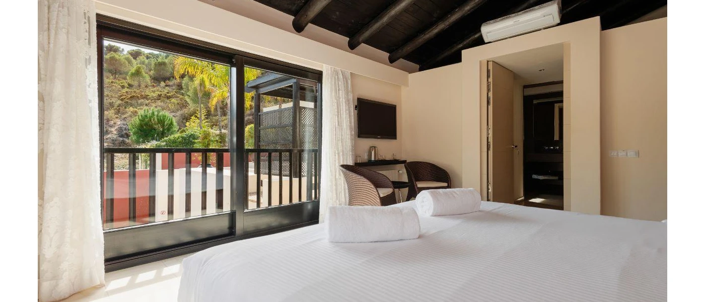 Hotel room with white bedding and cream walls, dark-wood ceiling and doors and a balcony
