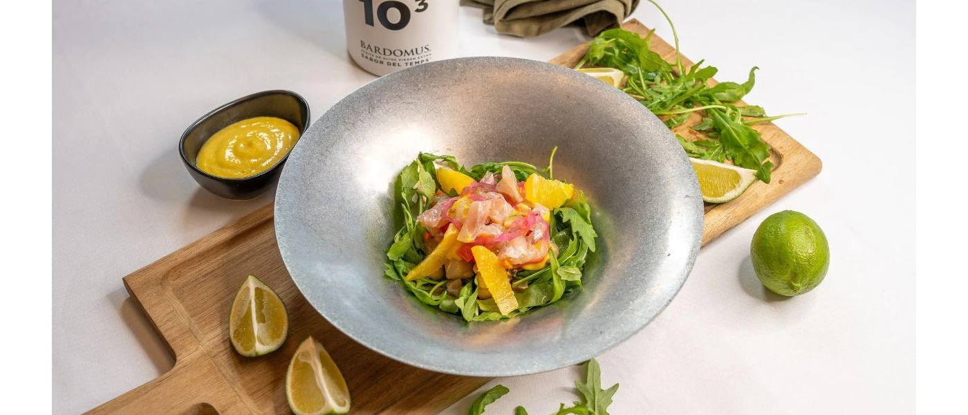 Grey bowl with a green salad and peppers, with limes on the side