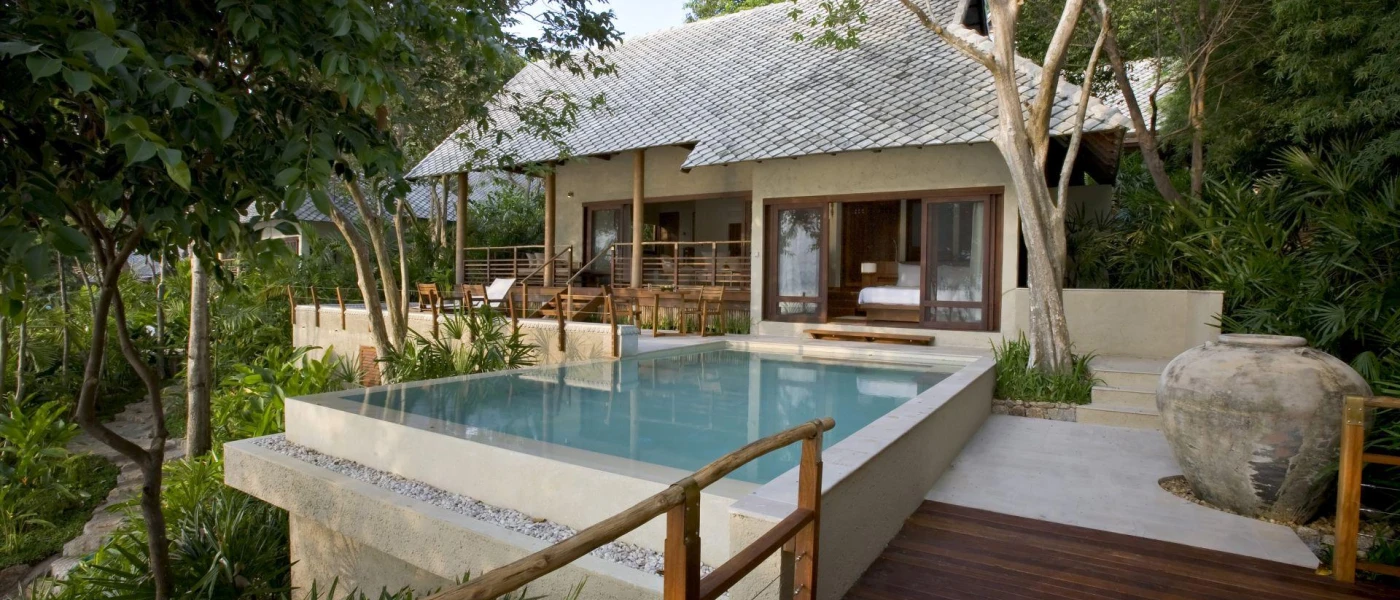 Villa with a tiled roof and private deck with a pool, shrouded by tropical plants