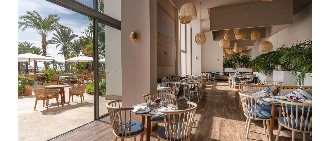 Airy restaurant with indoor and outdoor sections, rattan lantern lighting, blue cushioned chairs and glossy palm trees