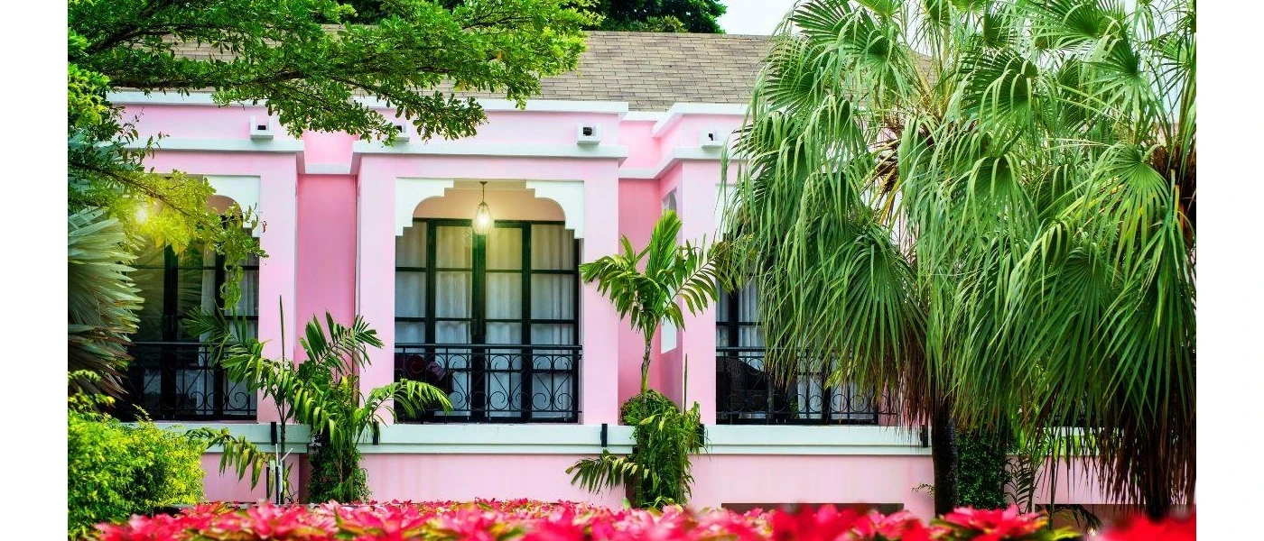 Pink building with large black windows surrounded by tropical greenery and pink flowers