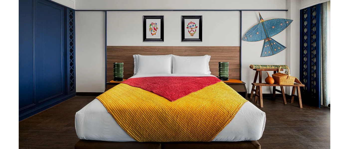 Modern bedroom with white bedding and a large red and gold throw, a navy painted wardrobe, wooden headboard and an intricate blue bird-shaped 3D wall mural