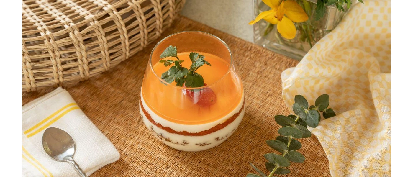Glass layered with a yoghurt-like substance and orange topping, with a herb garnish